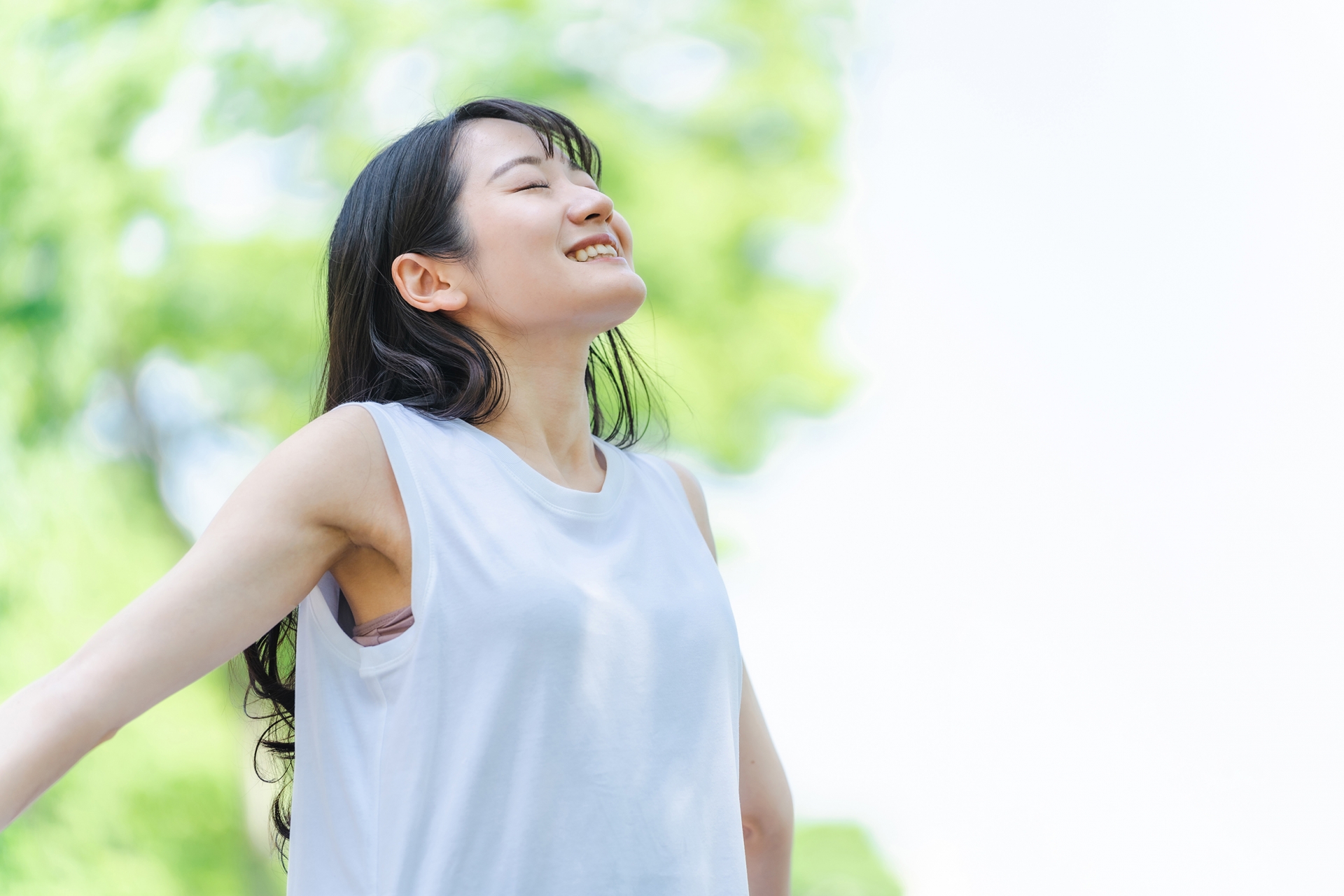 新緑の中で目を閉じて深呼吸している、笑顔の若い女性
