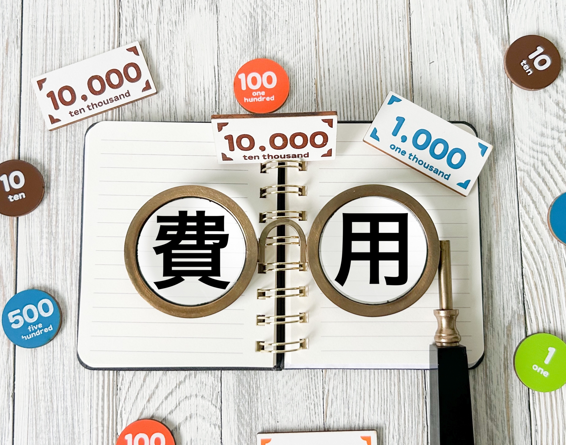 ノートに「費用」という漢字が書かれ、周りに金銭を表すチップが散りばめられている画像