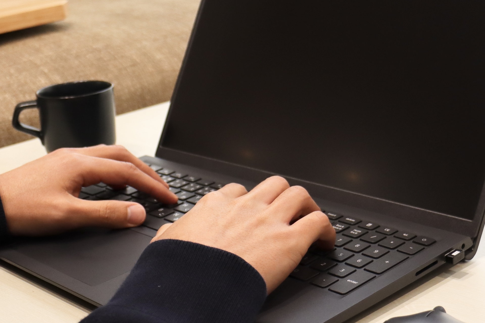 ノートPCでタイピングする手元と黒いコーヒーカップ