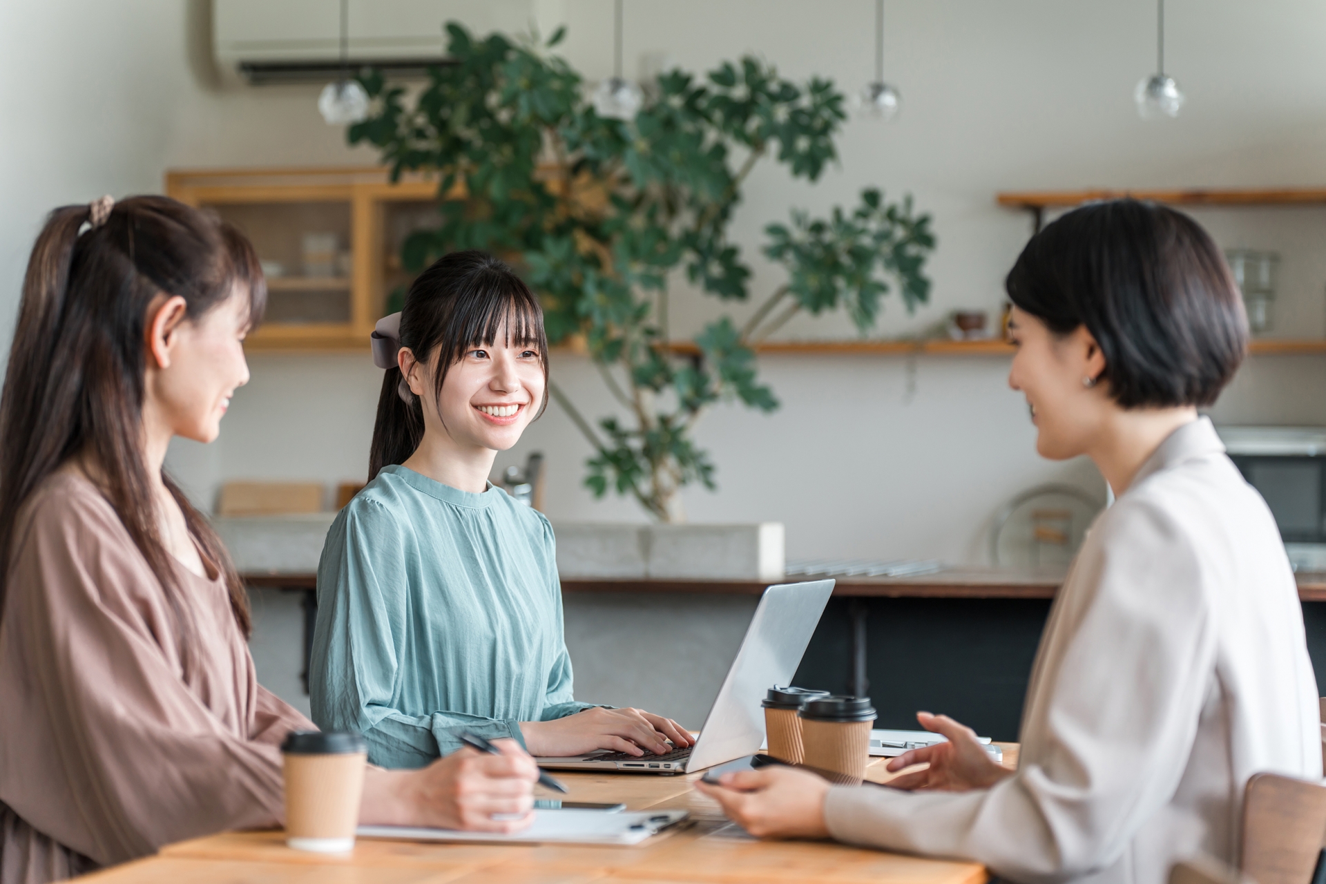 カフェ風オフィスで笑顔で打ち合わせをする3人の女性