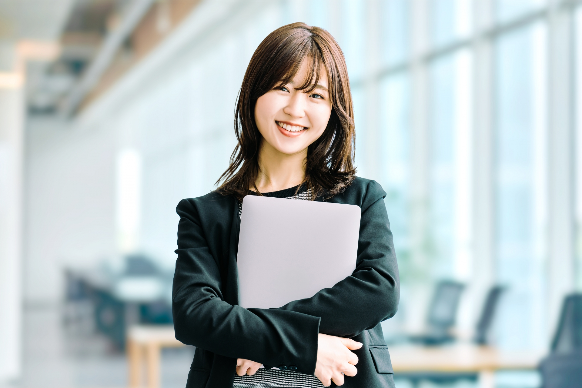 ノートPCを抱え笑顔を見せる女性ビジネスパーソン
