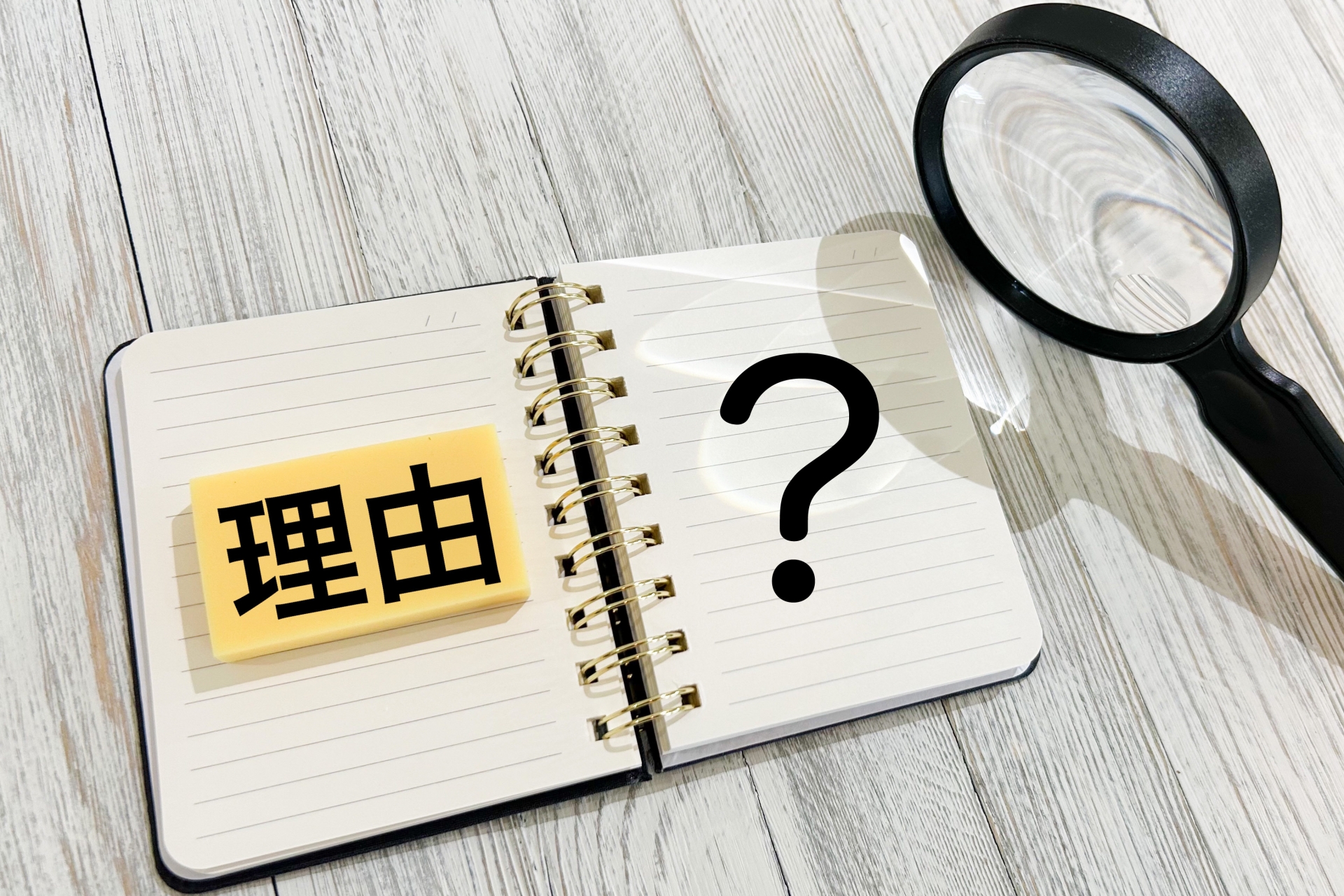 ノートに理由と書かれた付箋と疑問符を虫眼鏡で強調