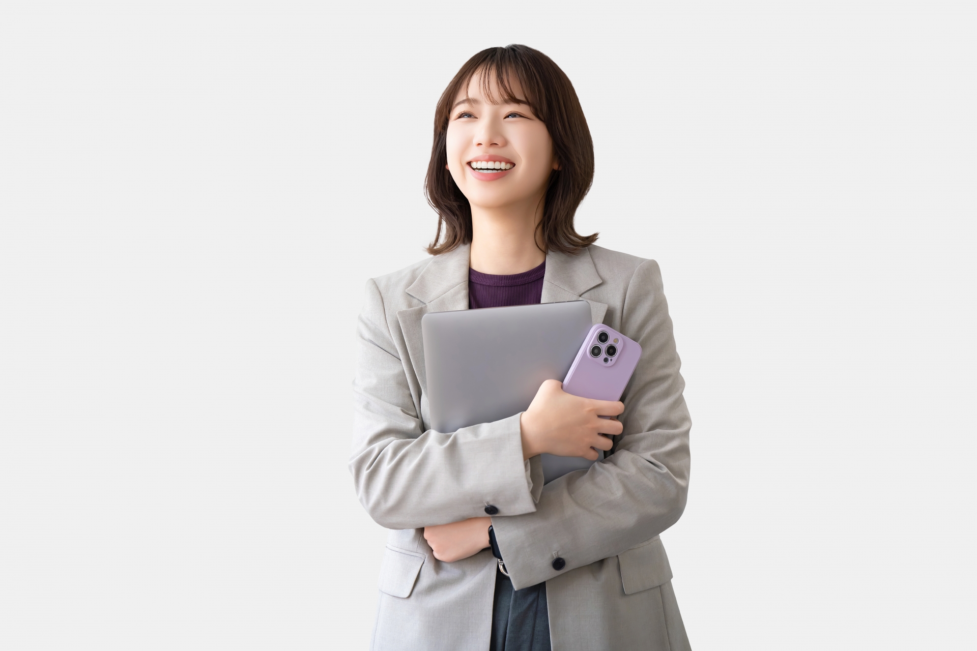ノートPCとスマホを抱え笑顔を見せる女性ビジネスパーソン